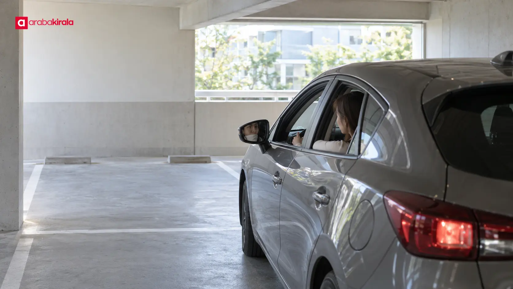 Kompakt otomobil kapalı otoparkta park yerine girerken sürücü çevresini kontrol ediyor
